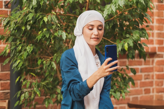 Giovane donna musulmana che indossa un foulard hijab in città che invia messaggi al cellulare