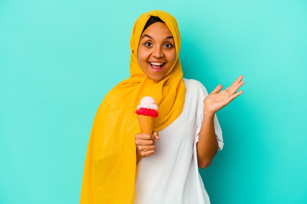 Giovane donna musulmana che mangia un gelato isolato sulla parete blu sorpresa e scioccata.