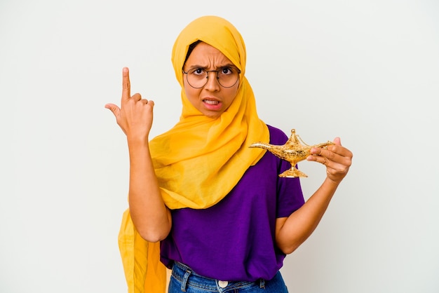 Giovane donna musulmana che tiene una lampada isolata sulla parete bianca che mostra un gesto di delusione con l'indice