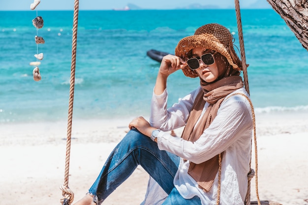 Giovane donna musulmana in vestito bianco che si siede sulla spiaggia nel giorno di vacanza. estate.