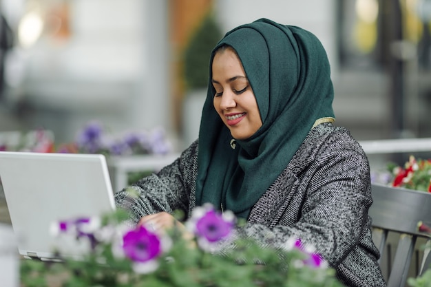 Giovane donna musulmana seduta in un caffè di strada e guardando in un laptop