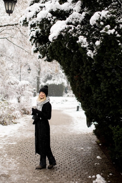 Giovane donna n vestiti caldi godendo nella neve con tazza di caffè da asporto