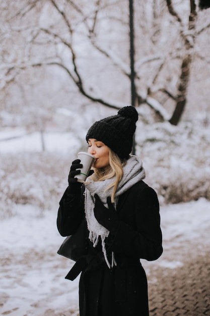 Giovane donna n vestiti caldi godendo nella neve con tazza di caffè da asporto