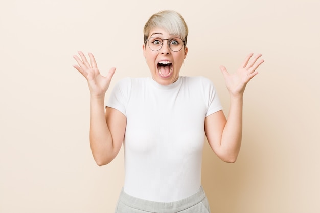 Giovane donna naturale autentica che indossa una camicia bianca che celebra una vittoria o un successo, è sorpreso e scioccato.