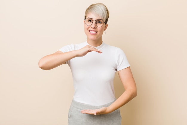 Giovane donna naturale autentica che indossa una camicia bianca che tiene qualcosa con entrambe le mani, presentazione del prodotto.