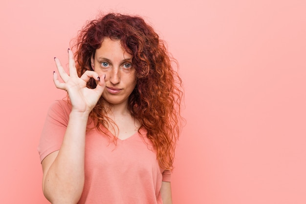 Giovane donna naturale e autentica rossa allegro e fiducioso mostrando gesto ok.