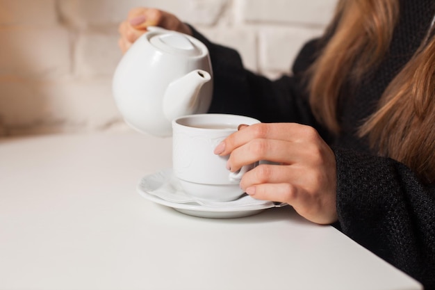 Giovane donna nel caffè che beve qui il tè della bevanda preferita in tazza bianca