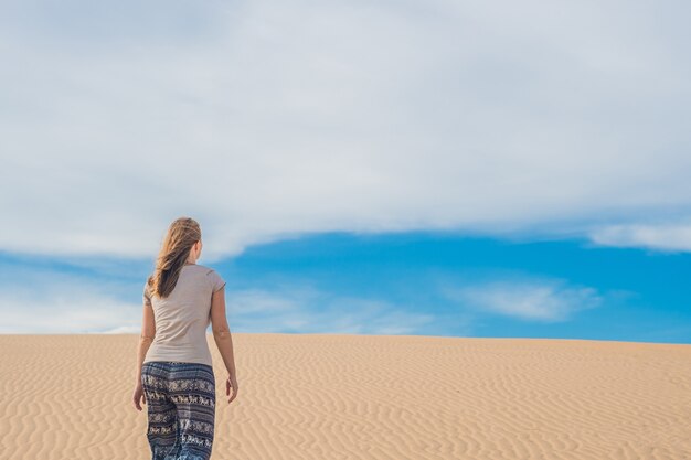 Giovane donna nel deserto sabbioso a piedi da sola contro il cielo nuvoloso tramonto