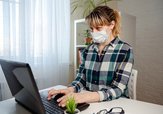 Giovane donna nel lavoro d'ufficio di lavoro della maschera medica dalla casa