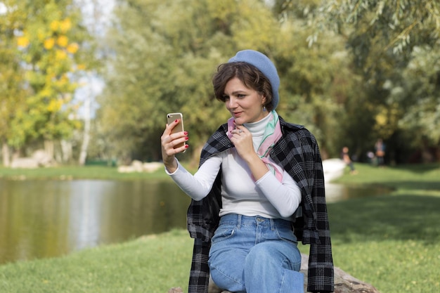 Giovane donna nel parco parla con il cellulare Ritratto di ragazza carina in stile francese
