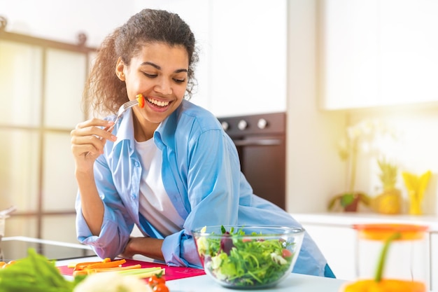 Giovane donna nella cucina di casa che mangia un'insalata genuina con verdure fresche