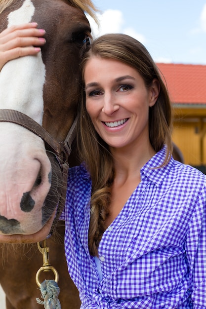 Giovane donna nella stalla con cavallo al sole