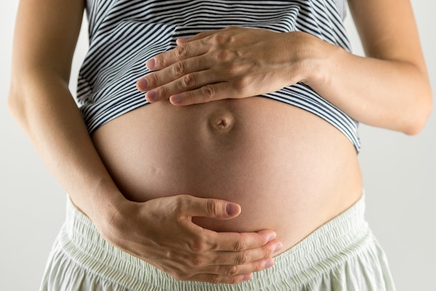 Giovane donna nelle ultime fasi della gravidanza che culla la sua pancia nuda con le mani mentre condivide un momento tenero con il suo bambino non ancora nato.