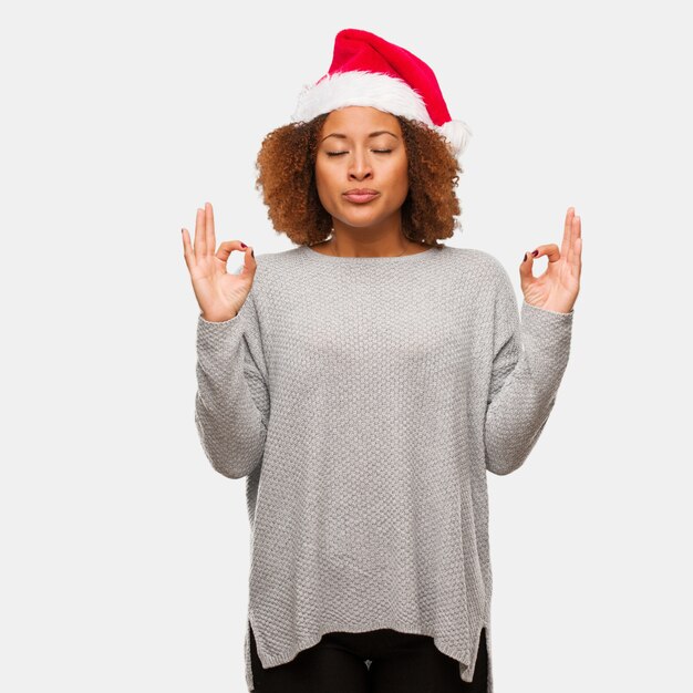 Giovane donna nera che indossa un cappello santa eseguendo lo yoga