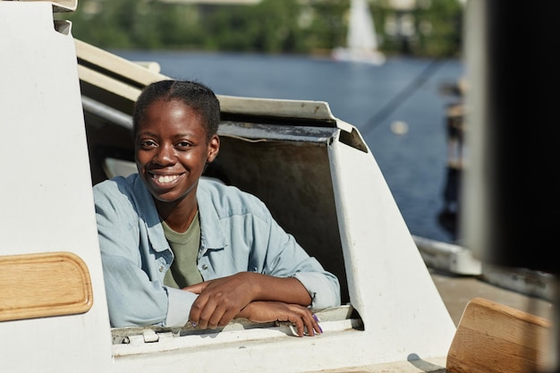 Giovane donna nera che sorride alla macchina fotografica che guarda fuori dalla finestra della barca