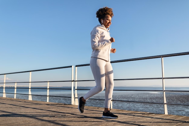 Giovane donna nera corsa al mare che fa jogging sul molo di legno vicino al mare