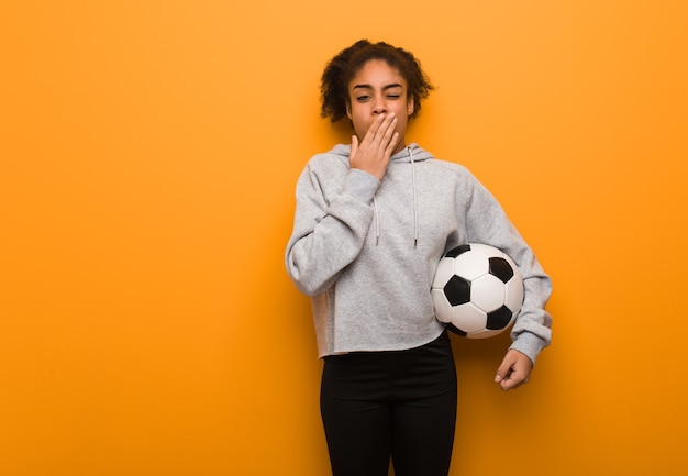 Giovane donna nera di forma fisica stanca e molto assonnata. Tenendo un pallone da calcio.