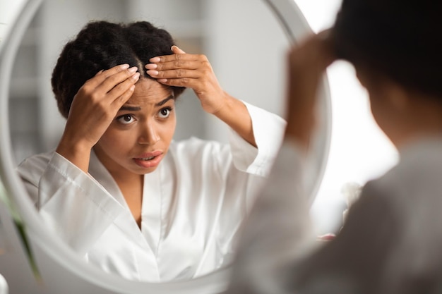 Giovane donna nera preoccupata che controlla le radici dei capelli a casa