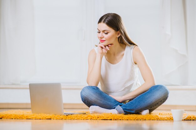 Giovane donna o studente felice con il computer portatile che si siede sul pavimento a casa