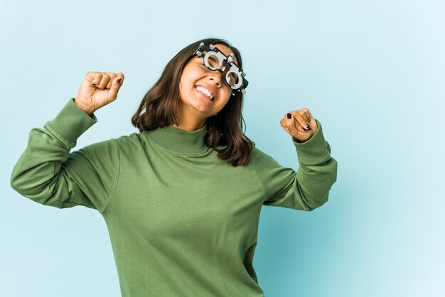 Giovane donna oculista sopra il muro isolato che celebra un giorno speciale, salta e alza le braccia con energia