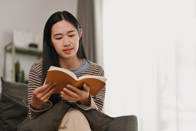 Giovane donna pacifica che legge un libro e si rilassa sul divano in un accogliente soggiorno