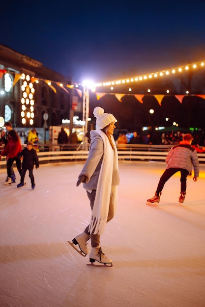 Giovane donna pattinaggio su ghiaccio su una pista in una festa di Natale la sera Luci intorno