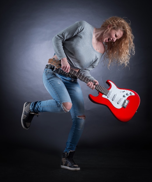 Giovane donna pazza con una chitarra che suona composizione jazz. isolato su un buio