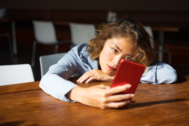 Giovane donna pensosa che pratica il surfing Internet sul telefono