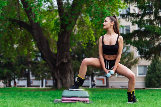 Giovane donna piacevole che si esercita sulla piattaforma a gradini nel parco