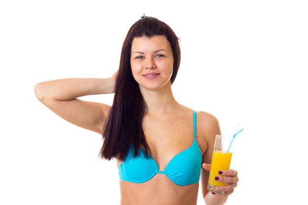 Giovane donna piacevole con lunghi capelli scuri in costume da bagno blu che tiene un cocktail giallo in studio