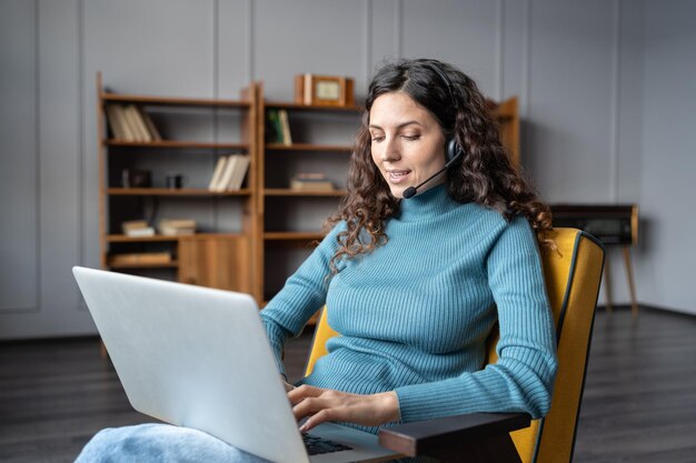 Giovane donna piacevole in cuffia utilizzando il laptop che parla con il partner tramite chat video da casa