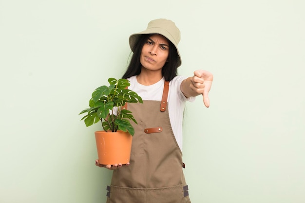 Giovane donna piuttosto ispanica che si sente crossshowing pollice verso il concetto di agricoltore o giardiniere