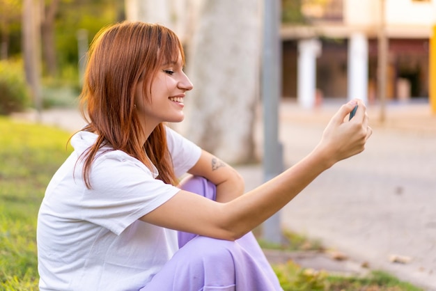 Giovane donna piuttosto rossa all'aperto utilizzando il telefono cellulare con un'espressione felice