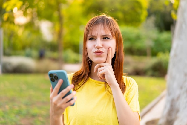 Giovane donna piuttosto rossa all'aperto utilizzando il telefono cellulare e il pensiero