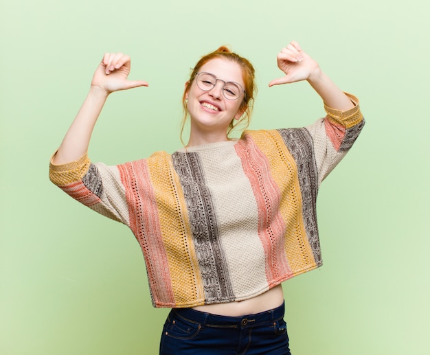 Giovane donna piuttosto rossa che si sente orgogliosa, arrogante e sicura di sé, che sembra soddisfatta e di successo, indicando se stessa contro la parete verde