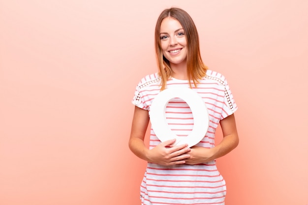 Giovane donna piuttosto rossa, eccitata, felice, gioiosa, con in mano la lettera O dell'alfabeto per formare una parola o una frase.