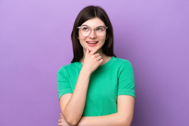 Giovane donna piuttosto russa isolata su sfondo viola con gli occhiali e il pensiero mentre si guarda in alto