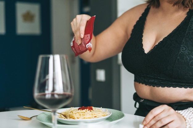 Giovane donna plus size corpo positivo con piatto di pasta e ketchup a pranzo a casa