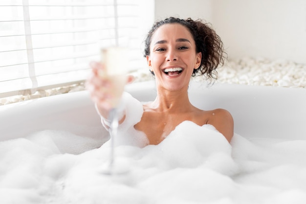 Giovane donna positiva che brinda con champagne che celebra le vacanze mentre ci si rilassa in un bagno schiumoso a