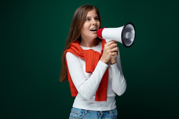 Giovane donna positiva che si lega un maglione rosso sulle spalle e parla in un altoparlante