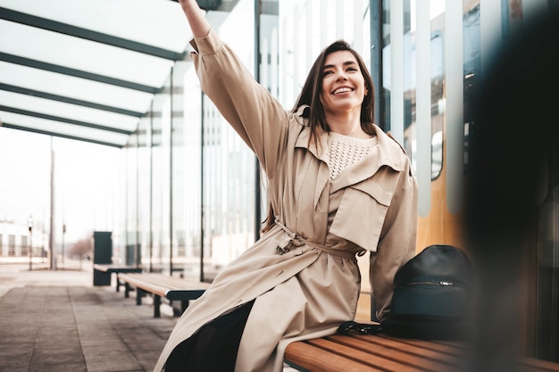 Giovane donna positiva che si siede ad una fermata e ad un ondeggiamento del trasporto pubblico