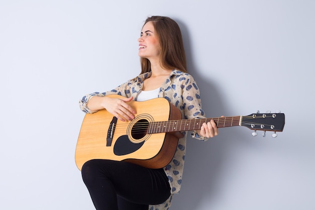 Giovane donna positiva con i capelli lunghi in giacca marrone che suona la chitarra in studio