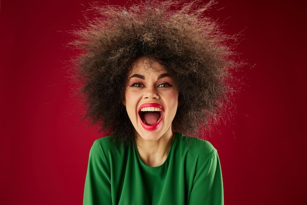 Giovane donna positiva con la smorfia di capelli ricci che posa il modello dello studio di emozione inalterato