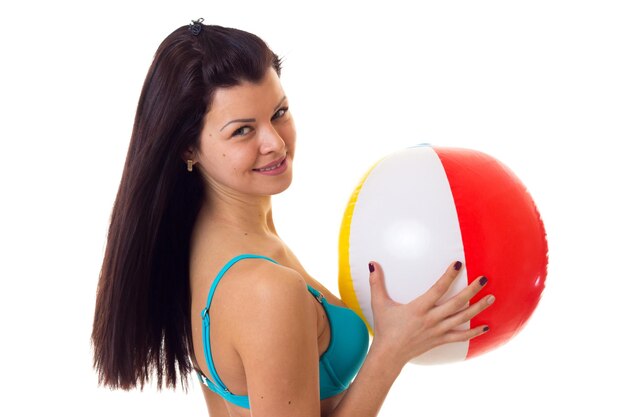 Giovane donna positiva con lunghi capelli scuri in costume da bagno blu che tiene grande palla in studio