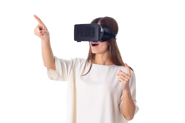 Giovane donna positiva in camicia bianca con occhiali per realtà virtuale su sfondo bianco in studio