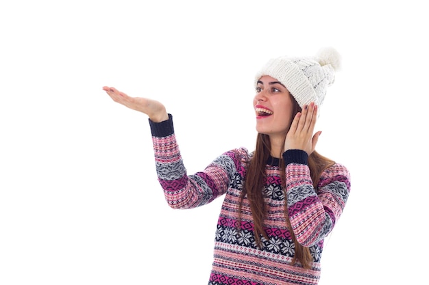 Giovane donna positiva in maglione viola e cappello bianco che tiene qualcosa su sfondo bianco in studio