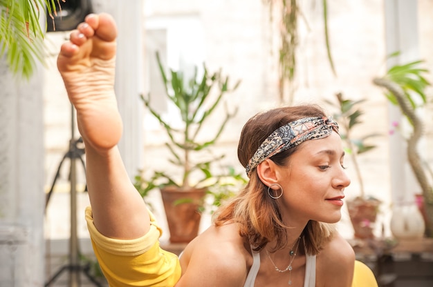 Giovane donna pratica yoga a casa tra i fiori.