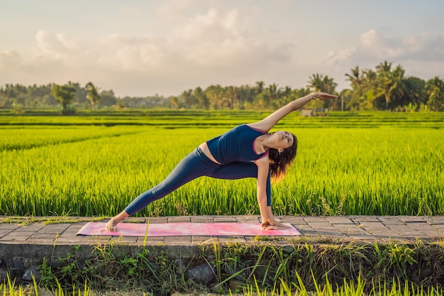 Giovane donna pratica yoga all'aperto nelle risaie al mattino durante il ritiro benessere a Bali