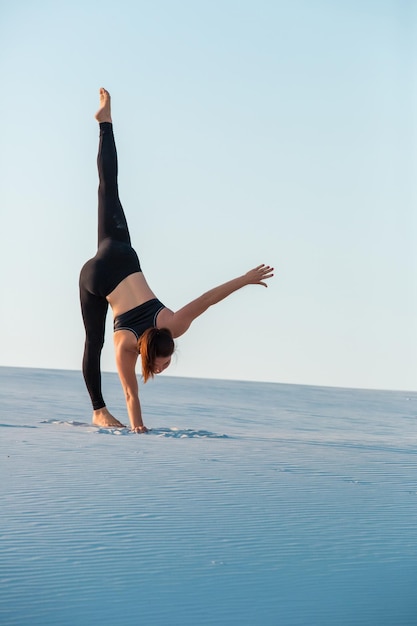 Giovane donna praticando inversione di bilanciamento posa yoga verticale sulla sabbia