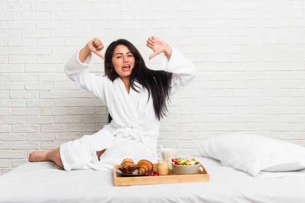 Giovane donna prendendo una colazione sul letto mostrando il pollice verso il basso ed esprimere antipatia.